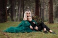 A beautiful blonde young woman in a long green dress and a diadem on her head with stylish young son in the forest. girl and boy Royalty Free Stock Photo