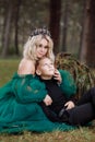 A beautiful blonde young woman in a long green dress and a diadem on her head with stylish young son in the forest. girl and boy Royalty Free Stock Photo