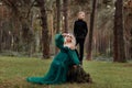 A beautiful blonde young woman in a long green dress and a diadem on her head with stylish young son in the forest. girl and boy Royalty Free Stock Photo