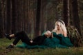 A beautiful blonde young woman in a long green dress and a diadem on her head with stylish young son in the forest. girl and boy Royalty Free Stock Photo