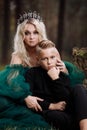 A beautiful blonde young woman in a long green dress and a diadem on her head with stylish young son in the forest. girl and boy Royalty Free Stock Photo