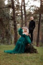 A beautiful blonde young woman in a long green dress and a diadem on her head with stylish young son in the forest. girl and boy Royalty Free Stock Photo