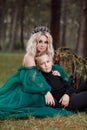 A beautiful blonde young woman in a long green dress and a diadem on her head with stylish young son in the forest. girl and boy Royalty Free Stock Photo