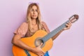 Beautiful blonde young woman playing classical guitar clueless and confused expression Royalty Free Stock Photo