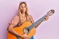 Beautiful blonde young woman playing classical guitar making fish face with mouth and squinting eyes, crazy and comical Royalty Free Stock Photo