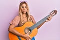 Beautiful blonde young woman playing classical guitar relaxed with serious expression on face Royalty Free Stock Photo