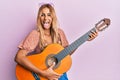 Beautiful blonde young woman playing classical guitar sticking tongue out happy with funny expression Royalty Free Stock Photo