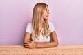 Beautiful blonde young woman wearing casual clothes sitting on the table looking to side, relax profile pose with natural face Royalty Free Stock Photo