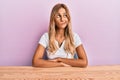 Beautiful blonde young woman wearing casual clothes sitting on the table smiling looking to the side and staring away thinking Royalty Free Stock Photo