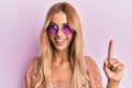 Beautiful blonde young woman wearing fashion pink sunglasses smiling with an idea or question pointing finger with happy face, Royalty Free Stock Photo