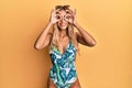 Beautiful blonde young woman wearing swimsuit and sunglasses doing ok gesture like binoculars sticking tongue out, eyes looking Royalty Free Stock Photo