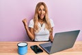 Beautiful blonde young woman working using computer laptop screaming proud, celebrating victory and success very excited with Royalty Free Stock Photo