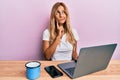 Beautiful blonde young woman working using computer laptop serious face thinking about question with hand on chin, thoughtful Royalty Free Stock Photo