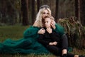 A beautiful blonde young woman in a long green dress and a diadem on her head with stylish young son in the forest. girl and boy Royalty Free Stock Photo