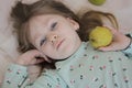 A beautiful blue-eyed girl lies with a green apple on the bed. Smiling girl. Royalty Free Stock Photo