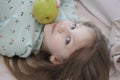 A beautiful blue-eyed girl lies with a green apple on the bed. Smiling girl. Royalty Free Stock Photo