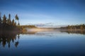 Beautiful blue lake with trees on a foggy morning in northern Minnesota at sunrise in September Royalty Free Stock Photo