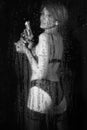 Blurred woman in lingerie and with a revolver in her hands behind wet glass with raindrops