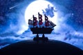 Beautiful boat toy over a blue balll with blurred blue full moon, stars and clouds scene at background