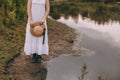 Beautiful boho girl standing at sunset near lake. attractive young woman in white bohemian dress with windy hair holding straw hat Royalty Free Stock Photo