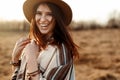 Beautiful boho woman hipster, smiling, wearing hat and poncho at sunset in mountains, true emotions, space for text Royalty Free Stock Photo