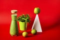 A beautiful bottle with a green smoothie stands on a red background, next to it stands a white geometric pyramid