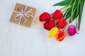 Beautiful bouquet of bright tulip flowers and gift box on white wooden background. Copy space Royalty Free Stock Photo