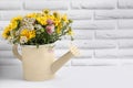 Beautiful bouquet of bright wildflowers in watering can on white wooden table near brick wall, space for text