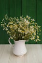 Beautiful bouquet of chamomiles in ceramic jug on white table against green wooden background Royalty Free Stock Photo