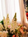 Beautiful bouquet of flowers with lupines in a vase on the background of curtains and white tulle in the living room or bedroom.