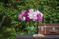 Beautiful bouquet of flowers with red, pink and white peonies and old suitcase, book on a wooden table in garden Royalty Free Stock Photo