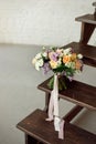 Beautiful bouquet of flowers of roses and lilac stands on a wooden ladder against a white brick wall. Royalty Free Stock Photo