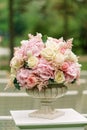 A beautiful bouquet of flowers in a stone vase stands on a column on a green background. Decor for the wedding ceremony Royalty Free Stock Photo