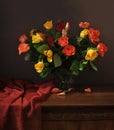 A beautiful bouquet of multicolored roses in a vase and a silk tablecloth on an antique wooden table. Still life Royalty Free Stock Photo