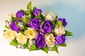 A beautiful bouquet of purple and yellow roses, green leaves and silver berries on a white surface. Top view. Royalty Free Stock Photo