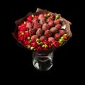 Beautiful bouquet of red roses and ripe strawberries in chocolate wrapped in brown paper on a black background Royalty Free Stock Photo