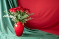 Beautiful bouquet of red roses in a red vase on the green and red textile background with copy space Royalty Free Stock Photo