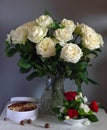 A beautiful bouquet of roses in a crystal jug and a box with tasty nuts. Royalty Free Stock Photo