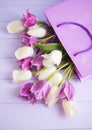 Beautiful bouquet of tender purple and white tulips in shopping bag on lilac wooden background
