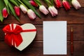 Beautiful bouquet of tulips on a dark wooden background with heart-shaped gift box, empty blank of paper and pen. Festive template Royalty Free Stock Photo