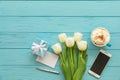 Beautiful bouquet of white tulips, blue gift box, cup of cappuccino, mobile phone on the blue wooden background with copy space, Royalty Free Stock Photo