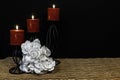 Beautiful bouquie of white roses, red candles perched on black candle holders on mesh place mat and wooden table with card and dar Royalty Free Stock Photo