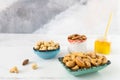 Beautiful bowls of different colors with roasted nuts cashews, almonds, hazelnuts and a glass jar with honey stand on a white
