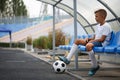 A teenager in a football uniform sitting on a blue bench on a stadium background. Sport, football and healthful concept.