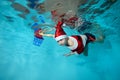 A beautiful boy is swimming underwater in a Santa Claus costume in the pool. He holds a new year`s lantern in his hand Royalty Free Stock Photo