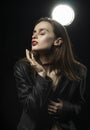 Beautiful braless girl with red lips, wearing an unbuttoned black blazer, touches her face with her hand on a dark background,