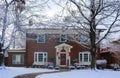 Beautiful brick house with bay windows with Christmas tree showing through and decorated pillars and sled on porch in snow framed