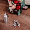 Beautiful bridal earrings and perfume on the wooden floor next to the wedding bouquet
