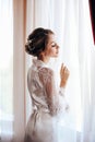 Beautiful bride with blond hair in elegant lace robe having morning preparation in wedding day