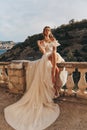 Beautiful bride with blond hair in luxurious wedding dress posing in balcony with beautiful view of mountains and sea Royalty Free Stock Photo